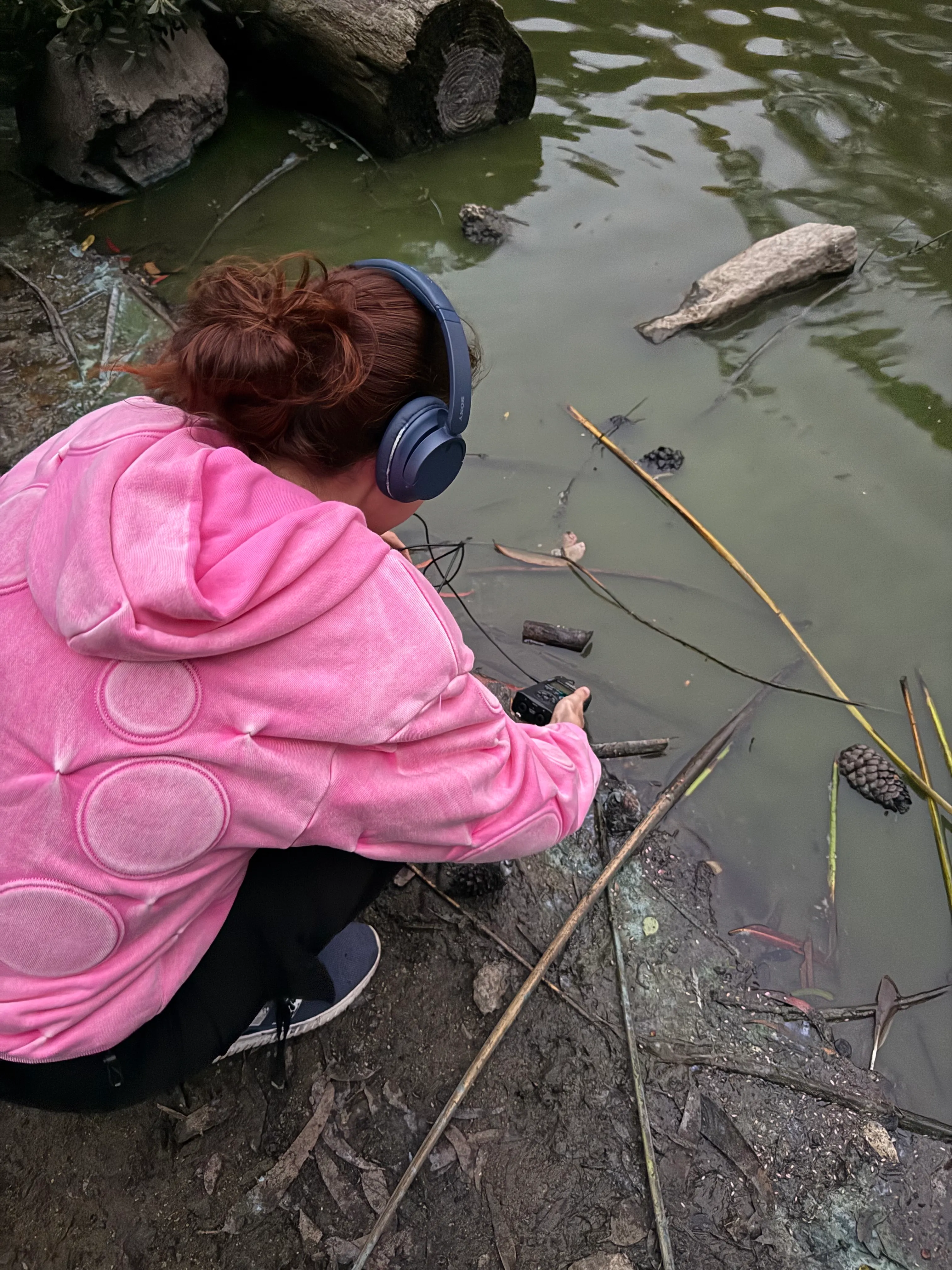 At a lake, field recorder in hand and headphones on.